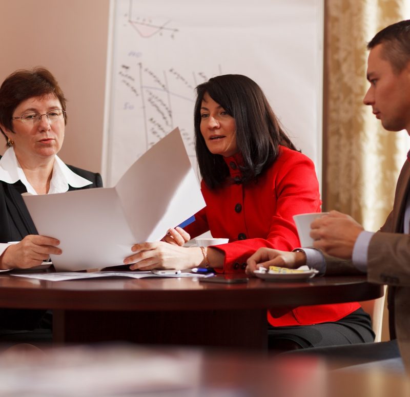 Businesspeople having a meeting over coffee sitting together at a table discussing a document, young man and two middle-aged women present